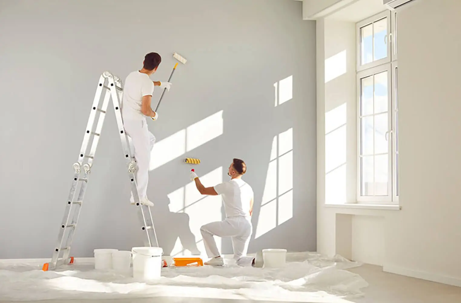 Two professional painters rolling gray paint on a large wall during a commercial painting project