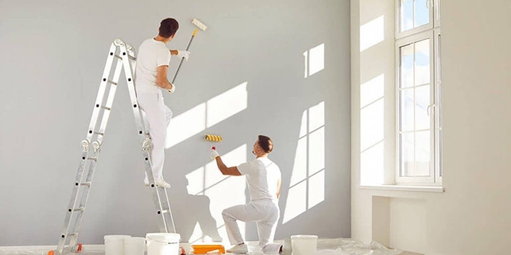 Two professional painters rolling gray paint on a large wall during a commercial painting project