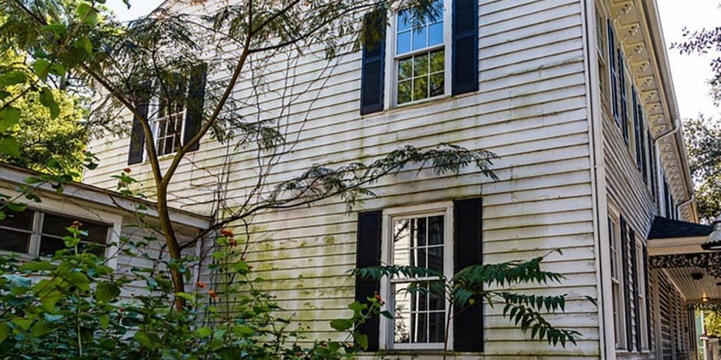 Weathered house exterior with mildew staining and failing paint on white siding